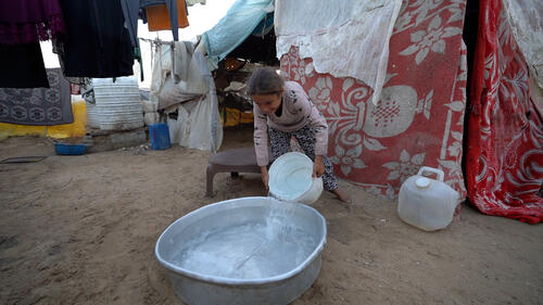 A girl pours water into a large bowl to wash her family's clothes in Gaza