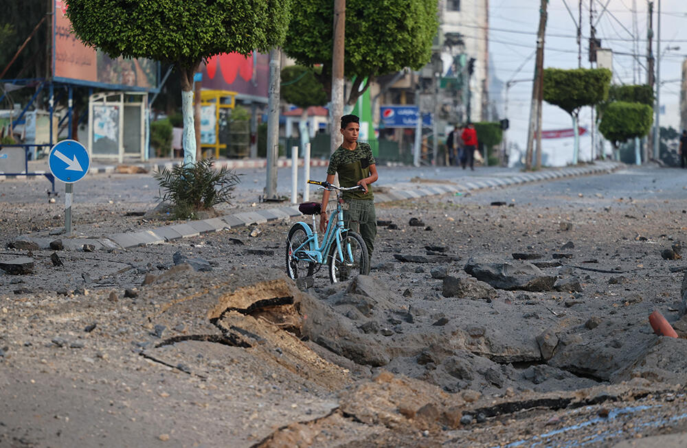 A Palestinian boy pushes his bicycle past a crater on the ground near the al-Sharouk tower after it was destroyed by an Israeli airstrike in Gaza City on 13 May 2021.