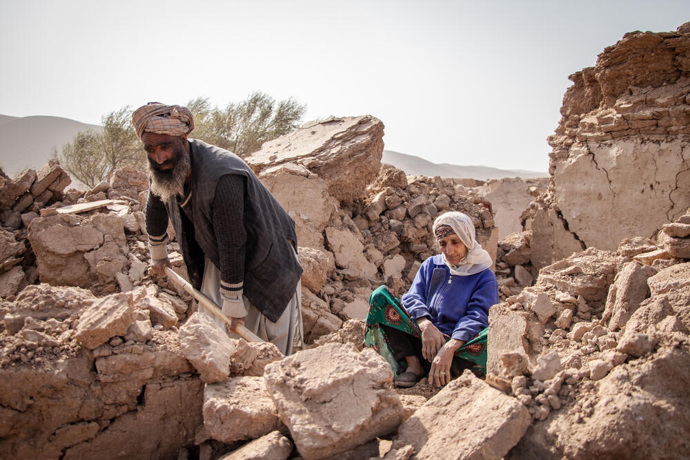 Abdul Salaam digging through the rubble of what used to be his home with a shovel. His mother seated on the side watches quietly.