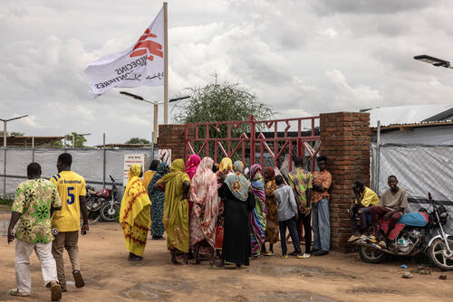 Women wait by a gate next to an MSF flag