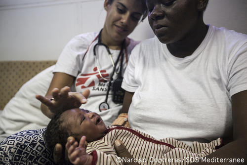 MSF Midwife Alice Gautreau, with newborn baby Christ and his Cameroonian mother. 
Baby Christ was born on the back of a crowded wooden boat on July 11, shortly before being rescued by the Aquarius. By the time MSF teams found them, mother and baby were still attached by umbilical cord and so they were promptly transferred onto the Aquarius and into the clinic, where the MSF Midwife Alice Gautreau and Doctor Craig Spencer helped to complete the delivery of the baby.
“In the clinic, we first separated mother and baby by cutting the umbilical cord.  Mum then needed a few stitches but other than that everything else went really well. Baby Christ weighs 7 pounds 10 ounces and against all odds, both mother and baby are doing really well,” she said.  
On July 11 2017, the Aquarius team rescued 630 people from two wooden boats and three rubber boats in distress, and took on board a further 230 people from Iuventa, the rescue boat of the NGO Jugend Rettet. Included in the 860 people on board are 9 pregnant women, 172 minors and newborn baby Christ. All 860 people were disembarked in Brindisi on July 14.