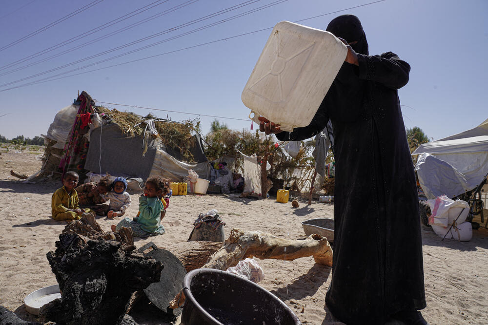 A woman pours out the last drops of water to prepare food for her young family at a displacement camp in Marib