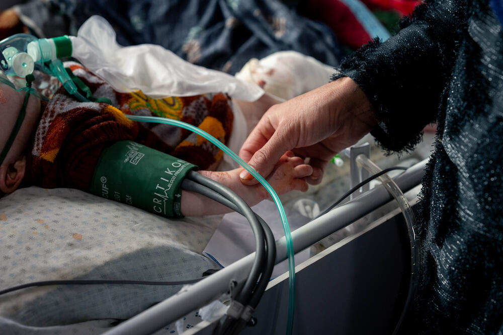 In an intensive care unit in a Kabul hospital, a mother holds the hand of Ekramullah, a severely malnourished young boy being cared for by MSF