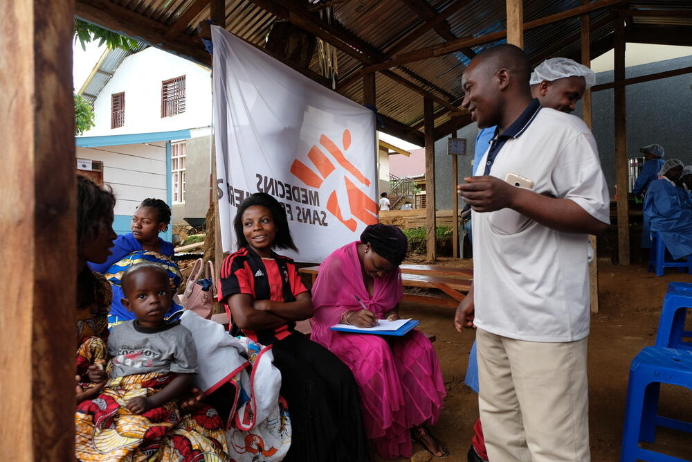 Community health worker Joseph talks with people waiting to receive the vaccination.
