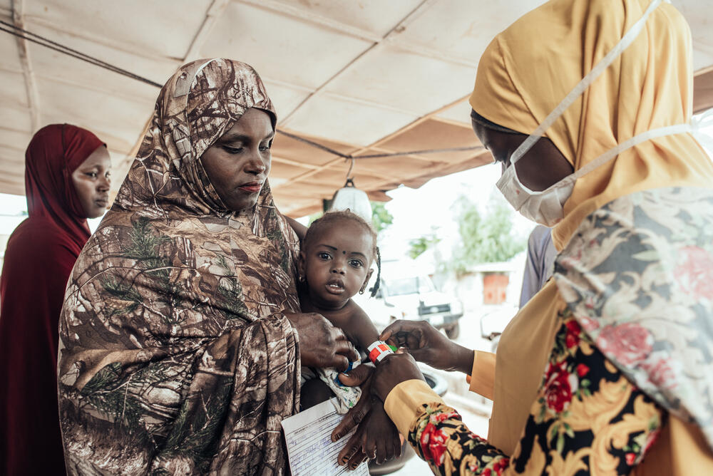 Sadiya Tukur holds her two-year-old daughter while a community healthcare worker checks for signs of malnutrition