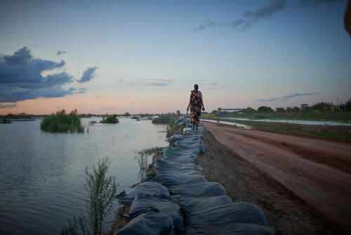 In South Sudan, a woman walks along the top of a dyke protecting Benitu camp - home to more than 100,000 displaced people