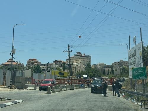 Photo of people waiting at the closed Israeli gate blocking a main road entrance to Hebron Photo of people waiting at the closed Israeli gate blocking a main road entrance to Hebron