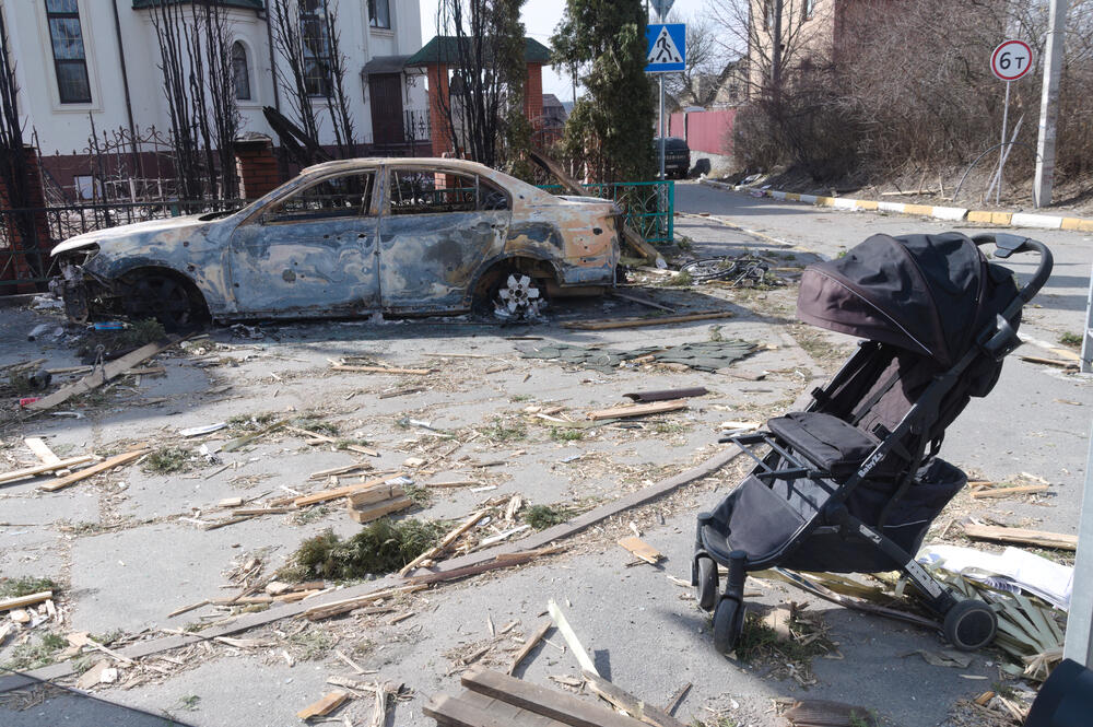 A stroller abandoned in the middle of a heavily-damaged street in Irpin