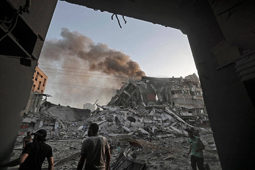 People gather amid the rubble in front of Al-Sharouk tower that collapsed after being hit by an Israeli air strike in Gaza City on 12 May 2021.