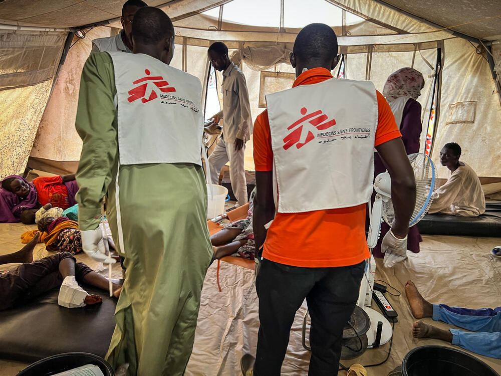 As thousands of Sudanese refugees arrive in Adré, Chad, MSF medical staff carry a war-wounded patient into a hospital tent
