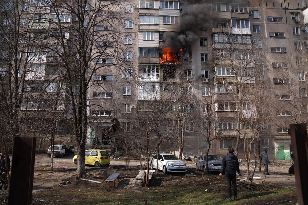 People look at a burning apartment building after shelling in Mariupol, Ukraine