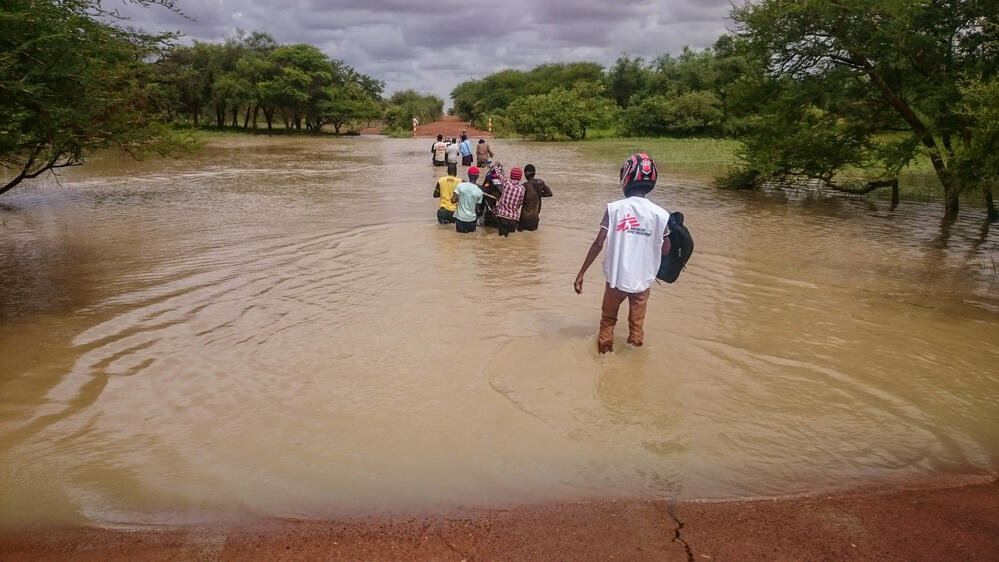 During the rainy season in Burkina Faso, roads become impassable, making access to healthcare even more difficult. Here, people help an MSF nurse cross a flooded roadway by carrying his motorcycle