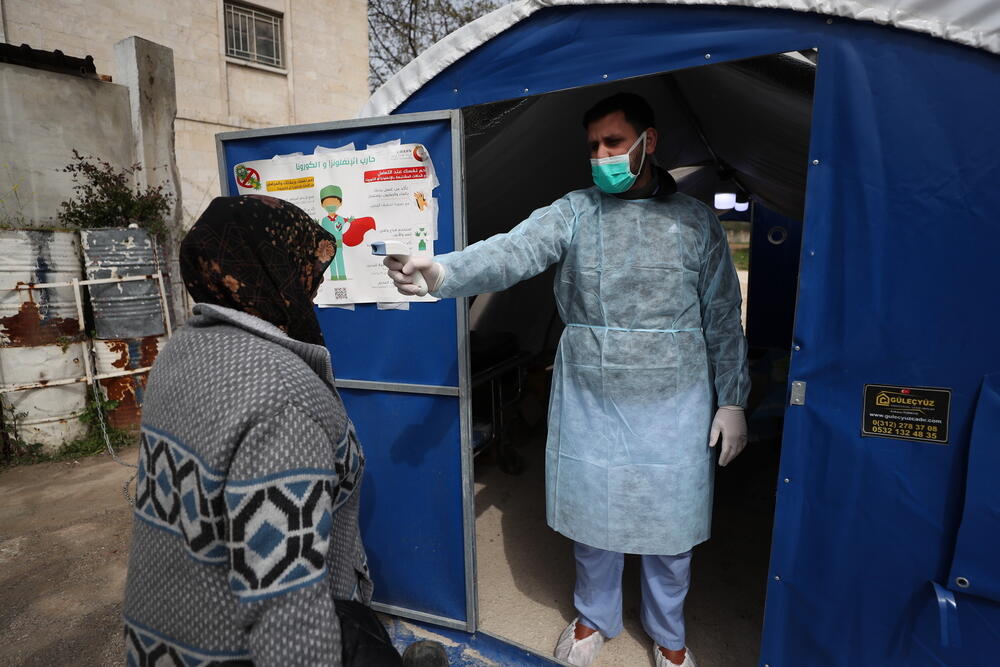 A doctor checks the temperature of a patient at the entrance of a dedicated space set up to identify potential COVID-19 patients outside a hospital supported by MSF in northwest Syria.
