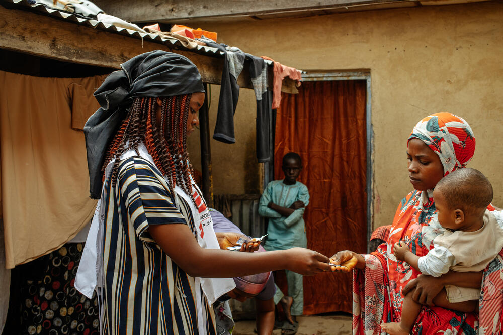 An MSF health promoter distributes water purification tablets to a mother in Magama village