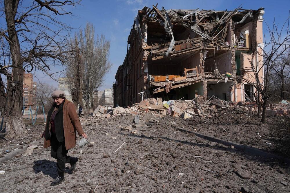 A woman walks past a building damaged by shelling in Mariupol, Ukraine