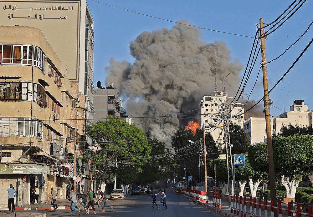 People run away from Al-Sharouk tower as it collapses after being hit by an Israeli airstrike in Gaza City on 12 May 2021.