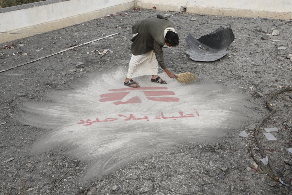 A man clears debris revealing the MSF logo painted on the roof of MSF's hospital
