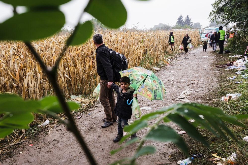 Malý chlapec ze Sýrie jde se svým otcem k přechodu Bapska. V pozadí v oranžových vestách stojí dobrovolníci z PomocUprchlikum.cz